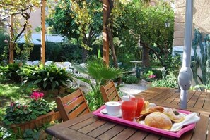 An outdoor dining area with wooden tables and chairs, surrounded by lush greenery and plants.