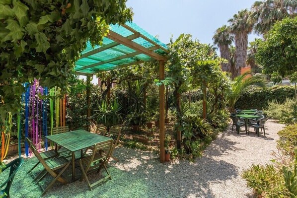 Une terrasse aménagée dans un jardin, avec une pergola en bois, une table et des chaises, ainsi qu’une variété de plantes en pot.