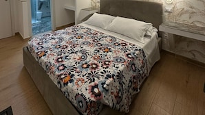 A bedroom with a bed, a nightstand, a wall-mounted light, a patterned wallpaper, and a door leading to a bathroom.