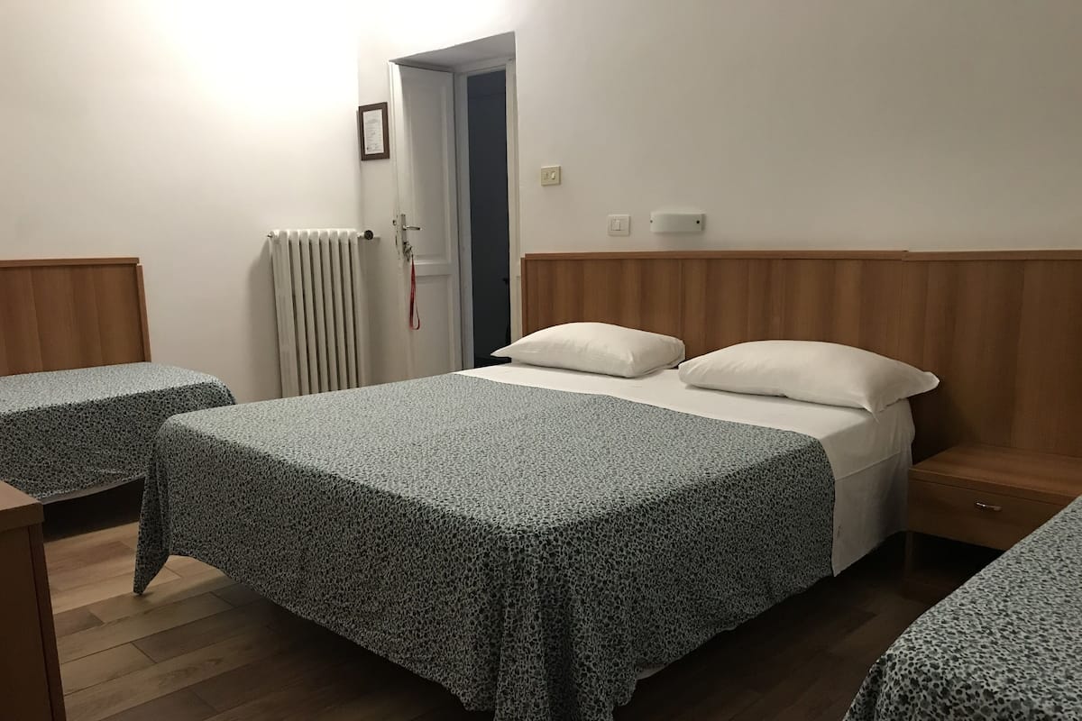 A room with a bed, a wooden nightstand, a bedside table, and a radiator.