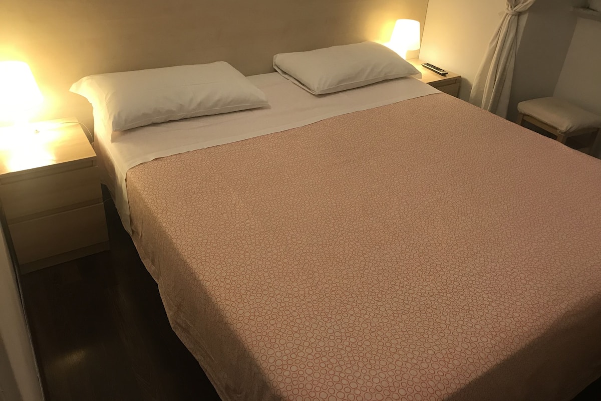 A neatly made bed with a patterned bedspread, two pillows, and a bedside lamp.