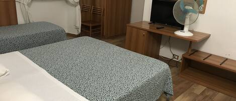 A bedroom with two beds, a wooden wardrobe, a desk with a TV and fan, and a mirror.