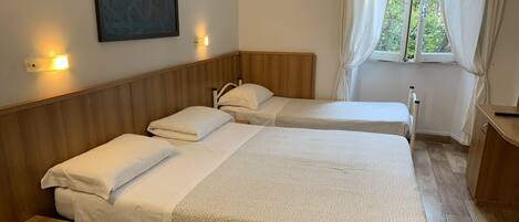 A hotel room with two beds, wooden headboards, a nightstand, a desk, and a window with curtains.