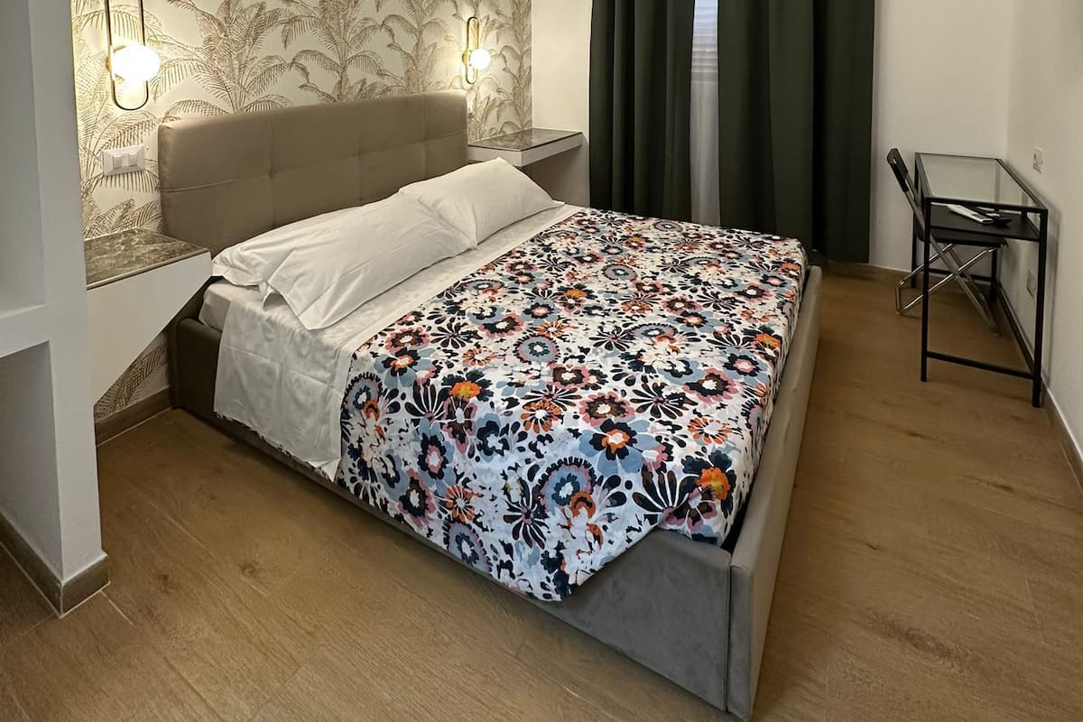 A bedroom with a bed, a desk, a TV, and a patterned wallpaper.