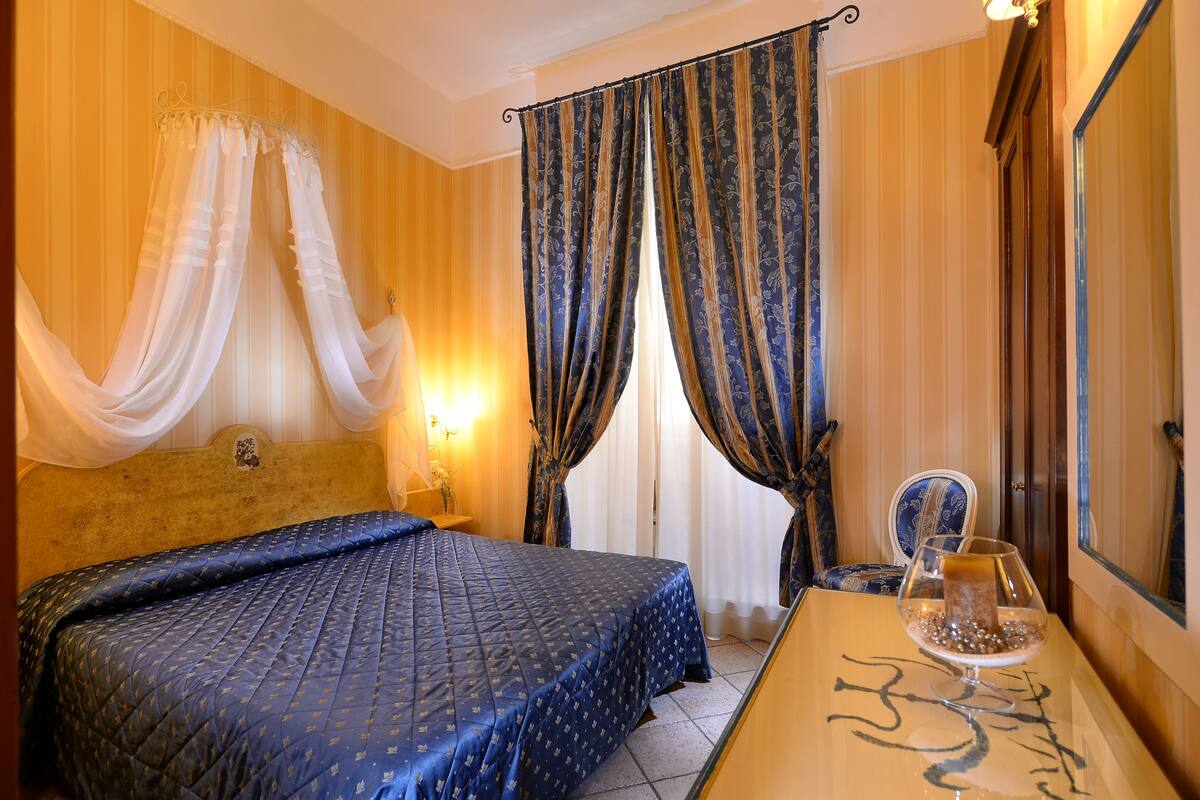 A hotel room with a bed, a bedside table with a glass of water, and curtains.