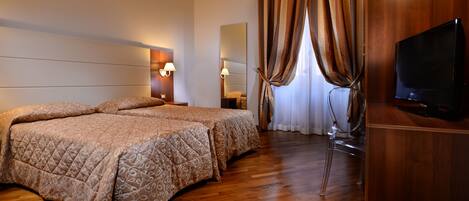 Habitación de hotel con dos camas, televisión, escritorio de madera, espejo y ventana con cortinas.