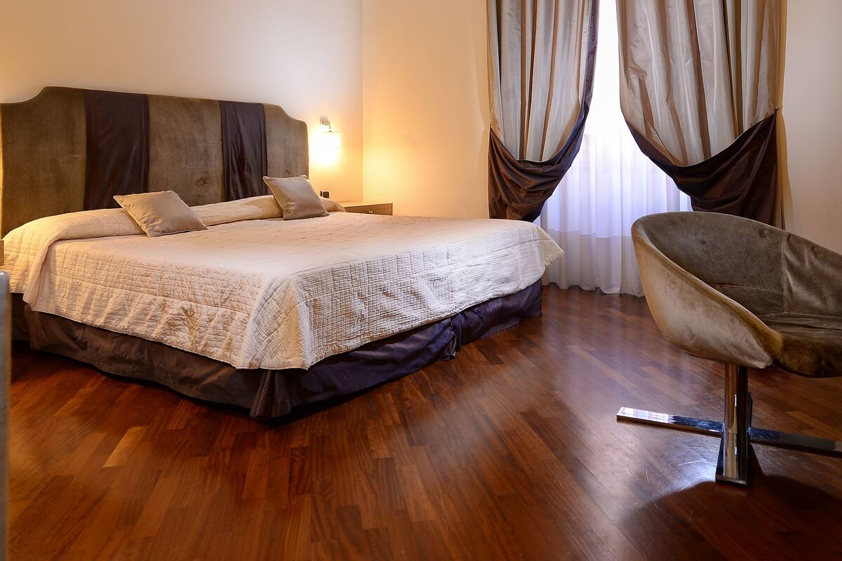 A hotel room with a large bed, a chair, and a ceiling with intricate patterns.