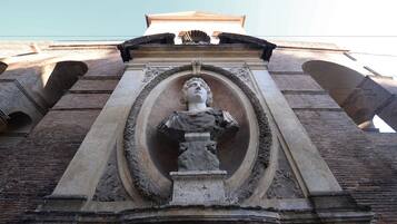 A classical architectural structure with a central statue, arched brickwork, and a flat roof.