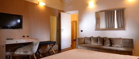 Habitación de hotel con cama, escritorio con silla, sofá, televisión y espejo.