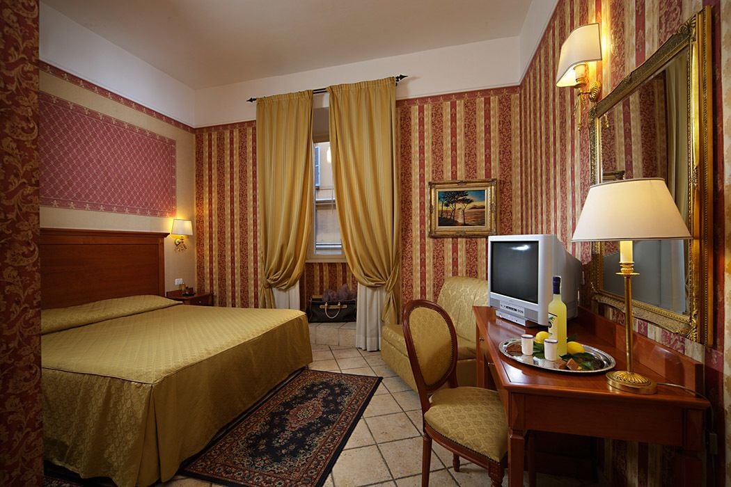 Une chambre d’hôtel avec deux lits, un bureau avec une télévision, une chaise, une lampe de bureau et un miroir décoratif.