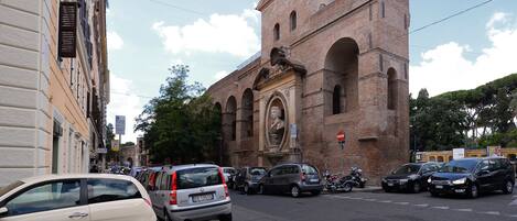 A street with parked cars and a historic building with a large archway and a statue.