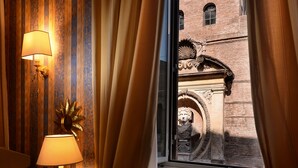 Habitación con papel tapiz a rayas, una lámpara y vistas a un edificio de ladrillo a través de una ventana con cortinas.