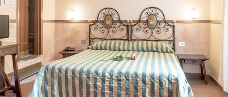 A neatly made bed with a striped bedspread and a single rose, a bedside table with a lamp, and a wooden nightstand.