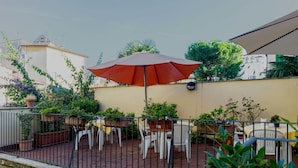 A terrace with outdoor seating, a large umbrella, and potted plants. - Hotel Monica (Florence)