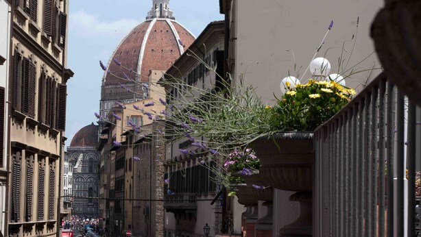 Vista da rua com edifícios históricos, uma cúpula imponente e um arranjo de flores.