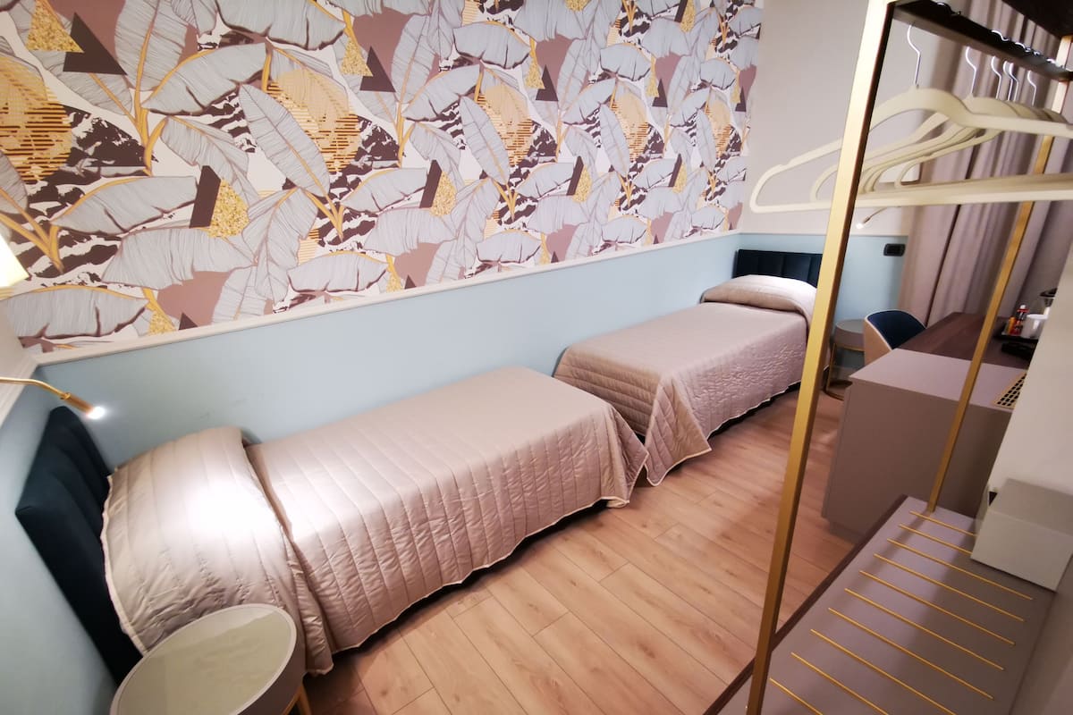 A hotel room with two single beds, a wooden floor, a wall with a leaf pattern, and a hanging clothes rack.