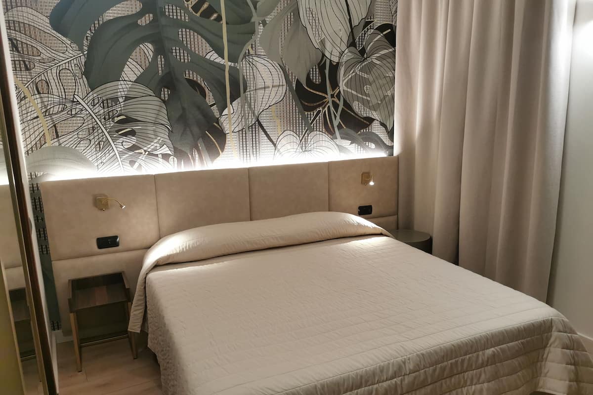 A bedroom with a large bed, a headboard with a leaf pattern, bedside tables, and a window with curtains.