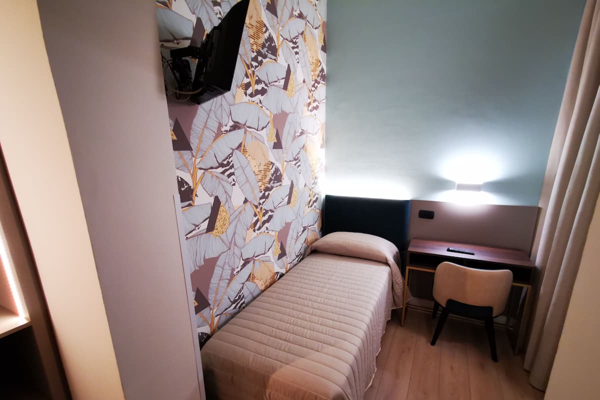 A small, compact room with a bed, a desk, and a chair.