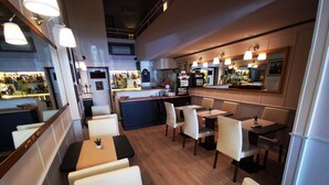 Um restaurante com cabines e mesas, uma área de bar e uma cozinha ao fundo.