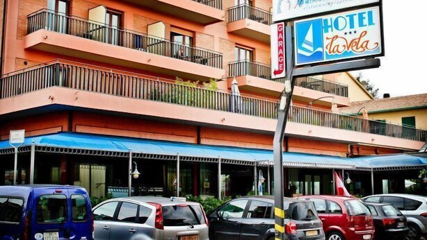 Un hôtel à plusieurs étages doté de balcons, une enseigne indiquant un garage et plusieurs voitures garées.