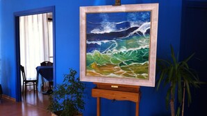 Ein Staffelei mit einem Gemälde von Meereswellen, ein Holzstuhl und zwei Zimmerpflanzen in einem Raum mit blauen Wänden.