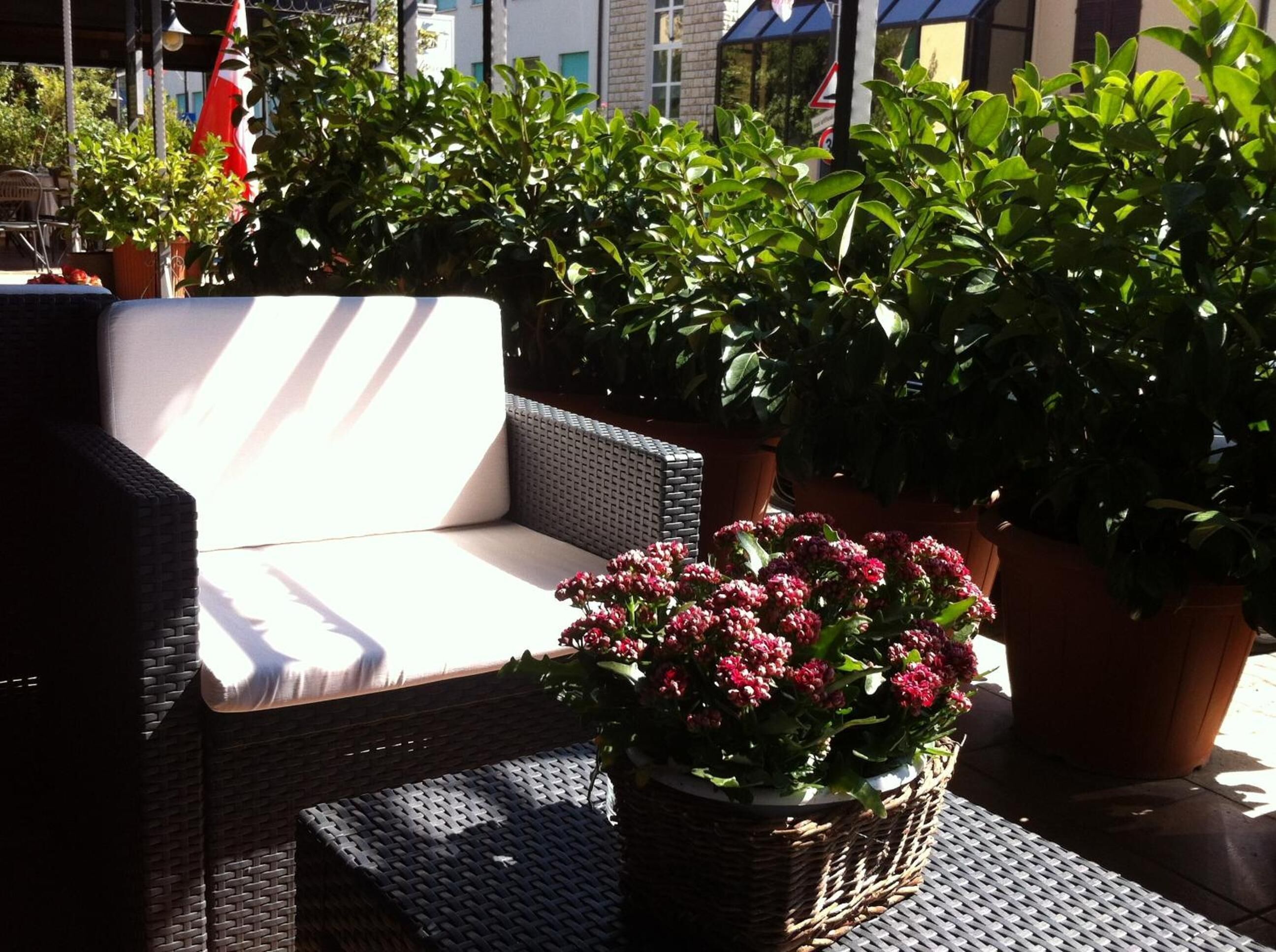 A wicker outdoor seating area with a cushioned bench, surrounded by potted plants and flowers.