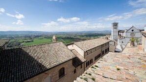 A historic building with a tiled roof, a bell tower, and a view of the surrounding countryside. - Hotel Properzio (Assisi)