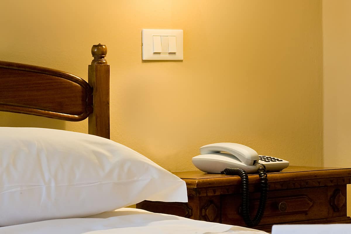 Quarto de hotel com cama, telefone ao lado e luminária fixada na parede.
