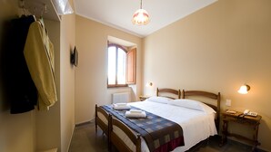 A neatly made bed with a quilt and two towels, a wooden nightstand with a lamp, and a window with curtains. - Hotel Properzio (Assisi)