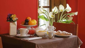 A breakfast table with a fruit bowl, coffee cups, a croissant, and a vase with flowers. - Hotel Properzio (Assisi)