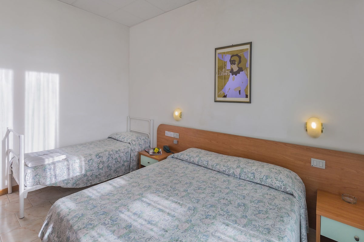 Une chambre d’hôtel avec deux lits, une tête de lit en bois, des lampes de chevet, une table de chevet et un tableau encadré au mur.
