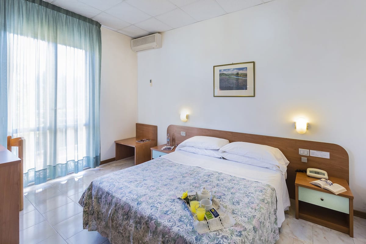 Une chambre d’hôtel avec un lit, des tables de chevet, un bureau et une fenêtre avec des rideaux.