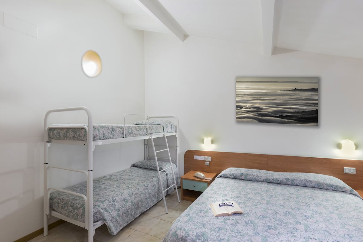 Une chambre de dortoir avec des lits superposés, une table de chevet avec une lampe et un tableau accroché au mur.