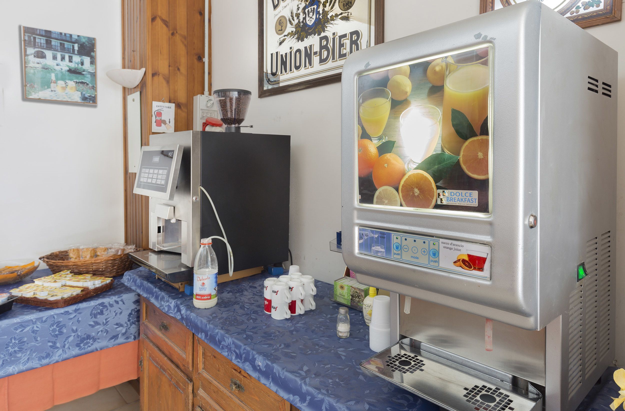 Una cucina con una macchina da caffè, un frigorifero e un distributore di succo di frutta.