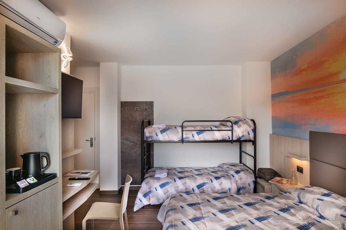 Une chambre avec des lits superposés, un bureau avec une chaise, une télévision et un tableau accroché au mur.