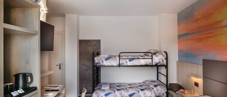 A room with bunk beds, a desk with a chair, a TV, and a painting on the wall.