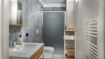 Un baño moderno con un lavamanos blanco, un inodoro, cabina de ducha y un perchero para toallas.
