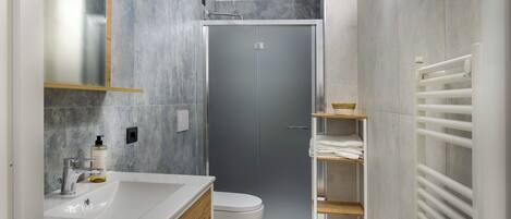 A modern bathroom with a white sink, a toilet, a shower enclosure, and a towel rack.
