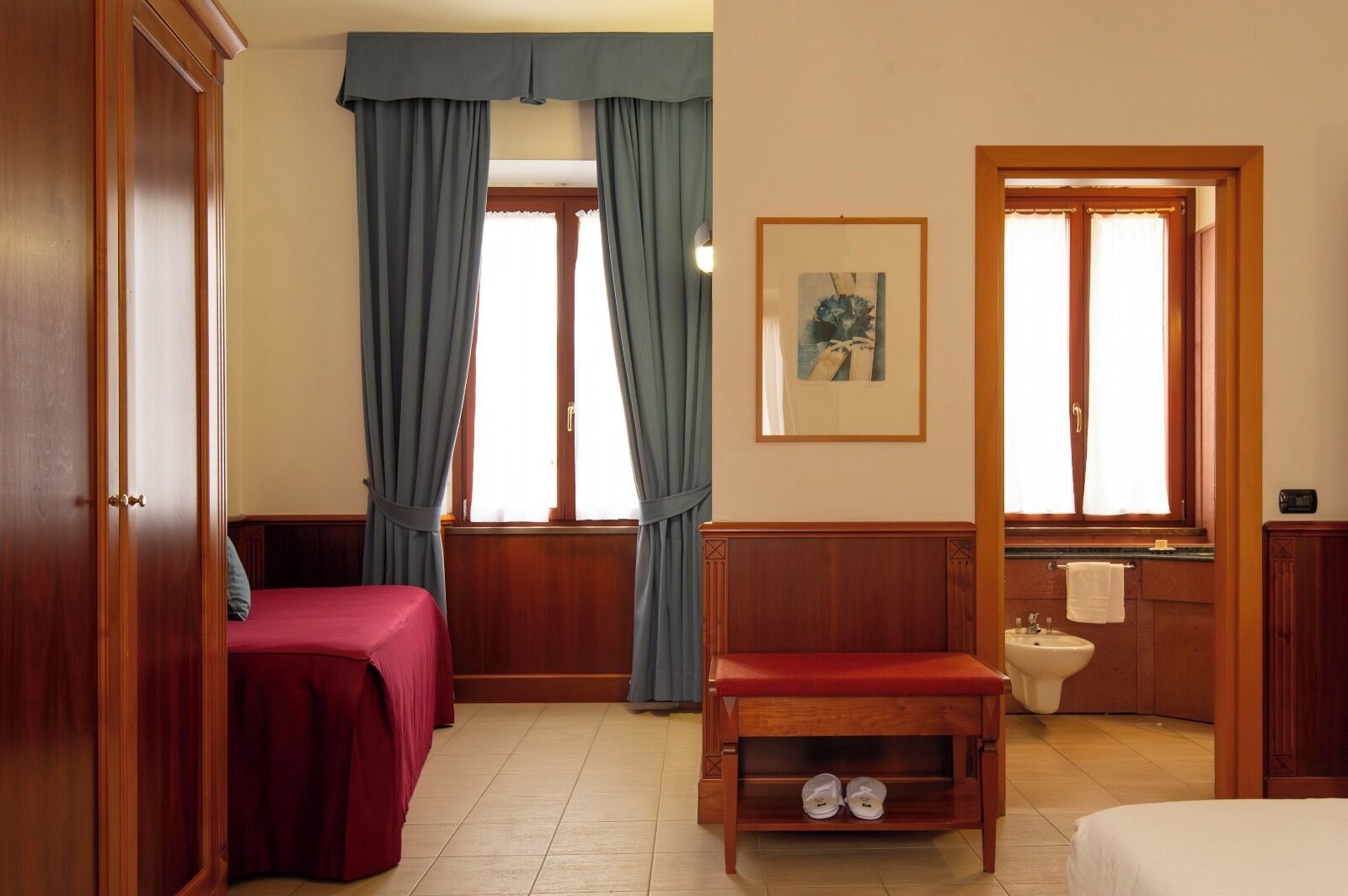 A room with two beds, a wooden bench, a sink, and a framed picture on the wall.