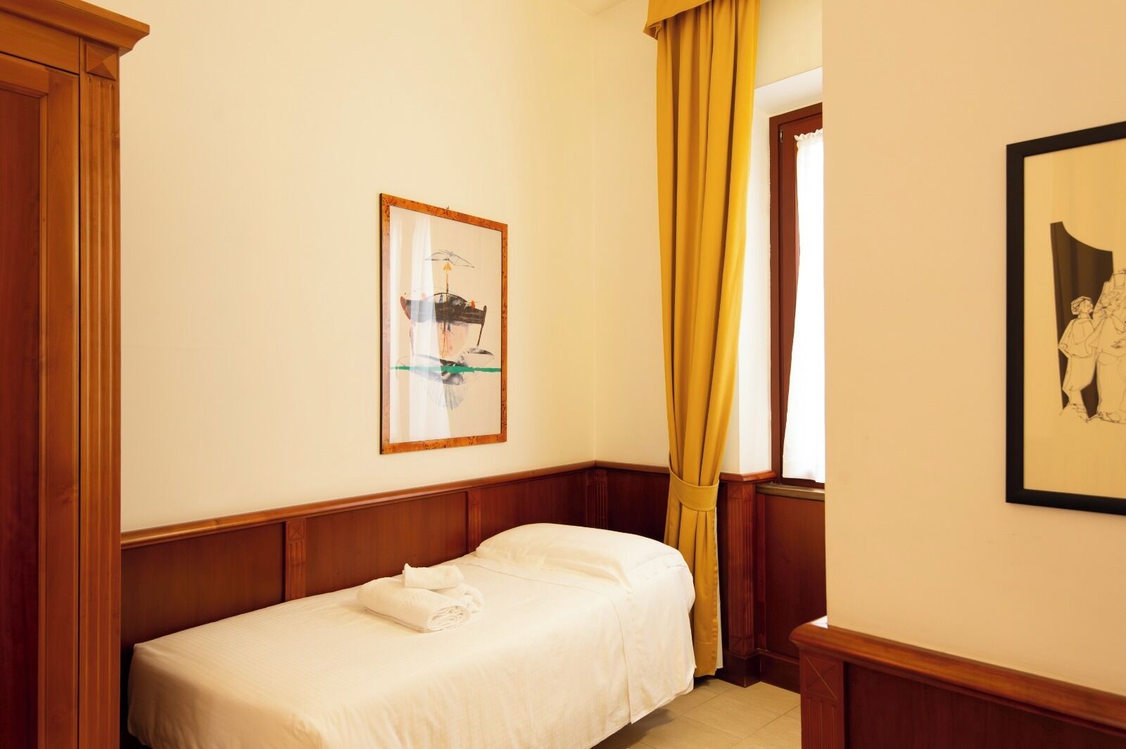 Uma cama de solteiro num quarto com painéis de madeira, um quadro na parede e uma janela com cortinas amarelas.