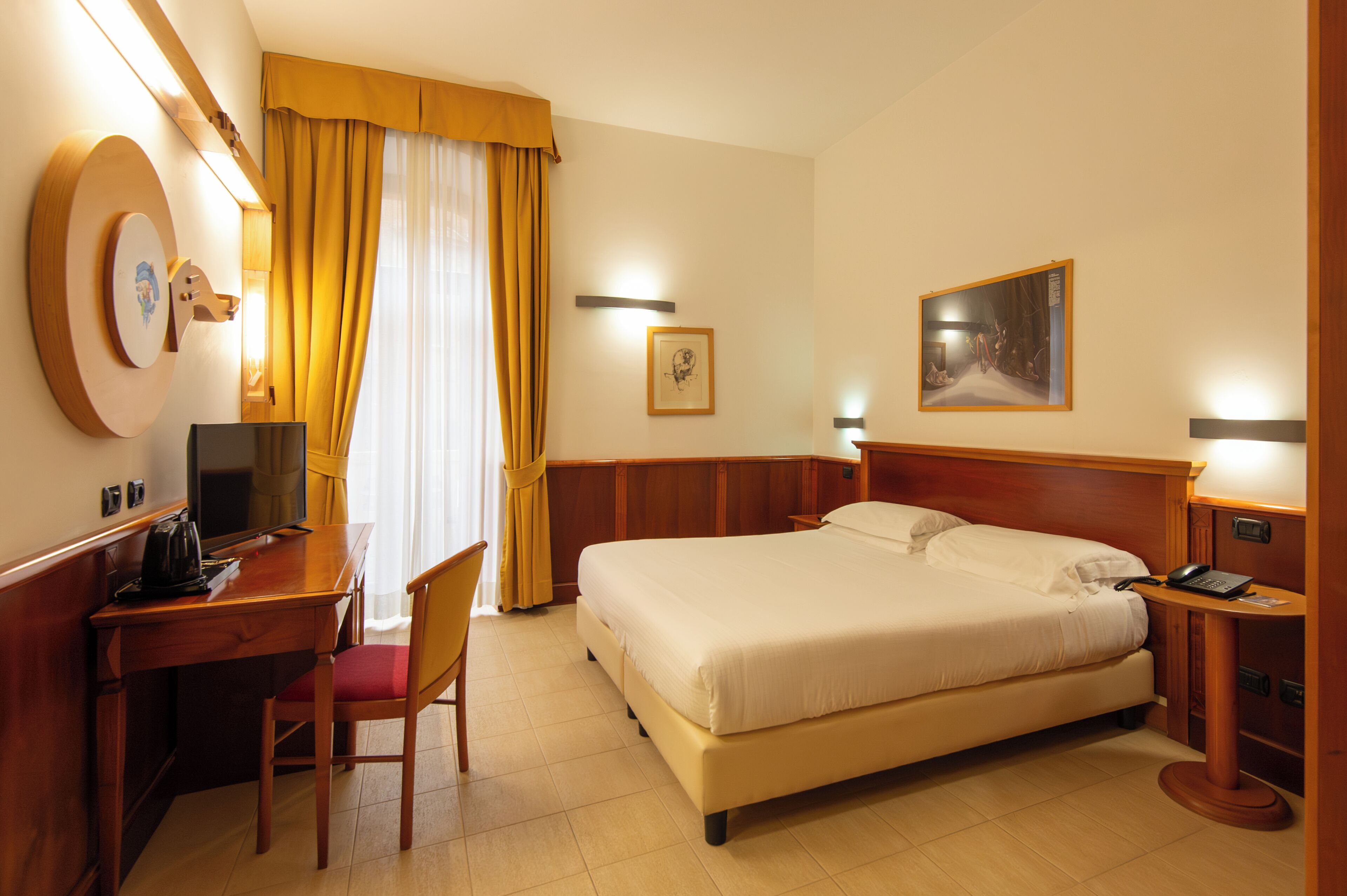 A hotel room with a bed, desk, chair, and a television.