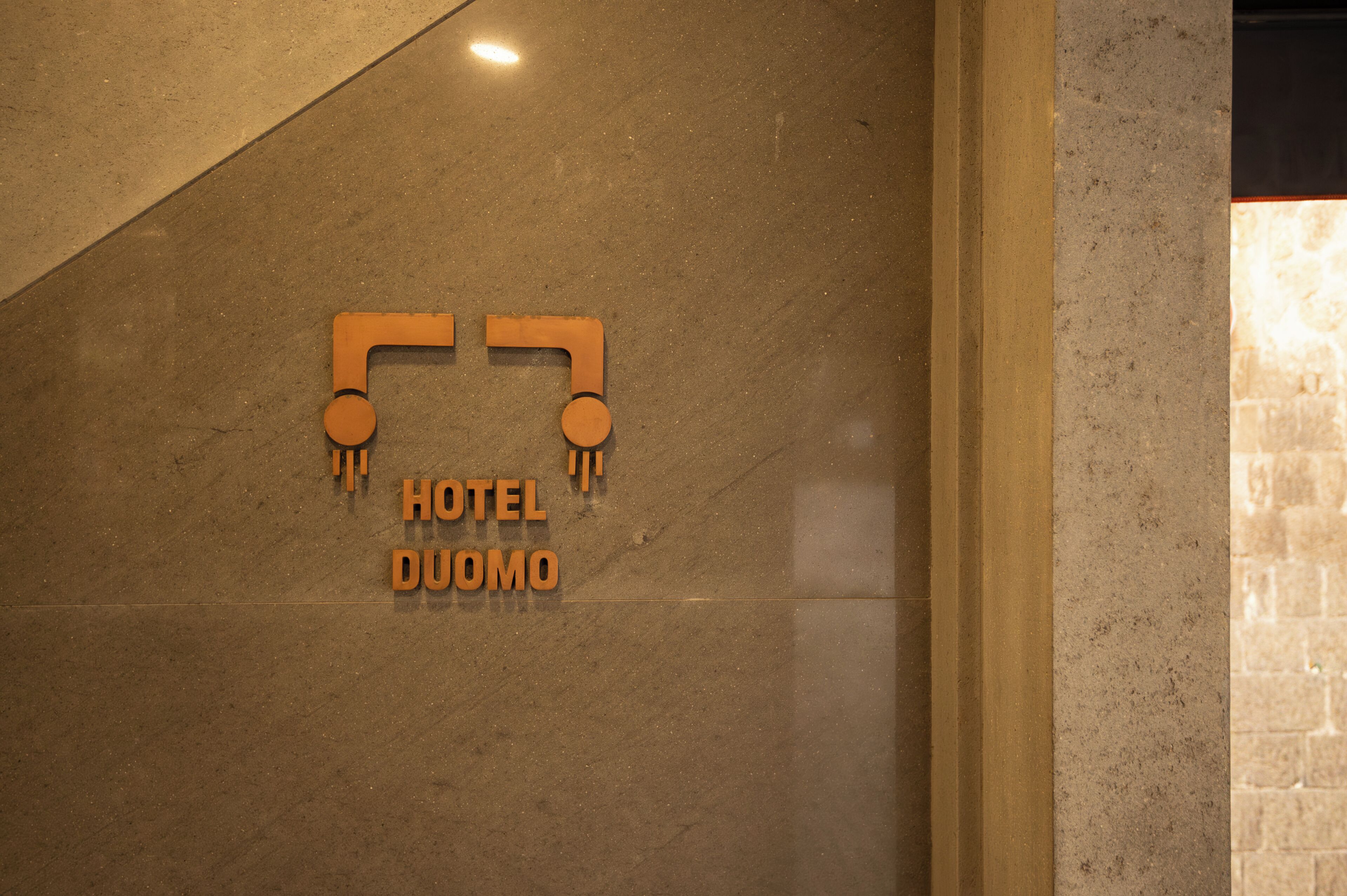 Un letrero de hotel con el nombre 'HOTEL DUOMO' sobre una pared de mármol.
