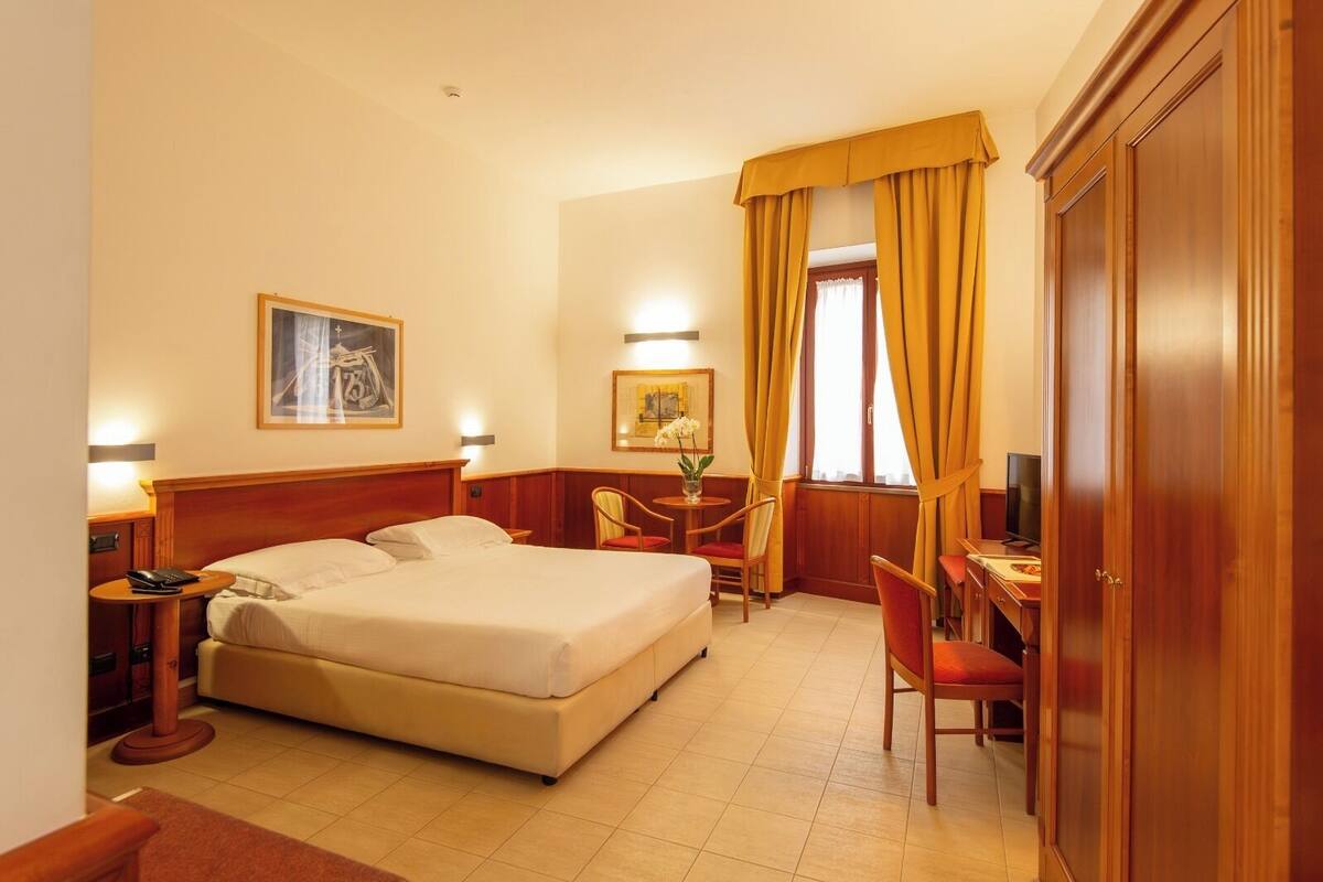 Une chambre d’hôtel comprenant un lit, une table de chevet, une lampe, une chaise, un bureau, une télévision et une armoire.
