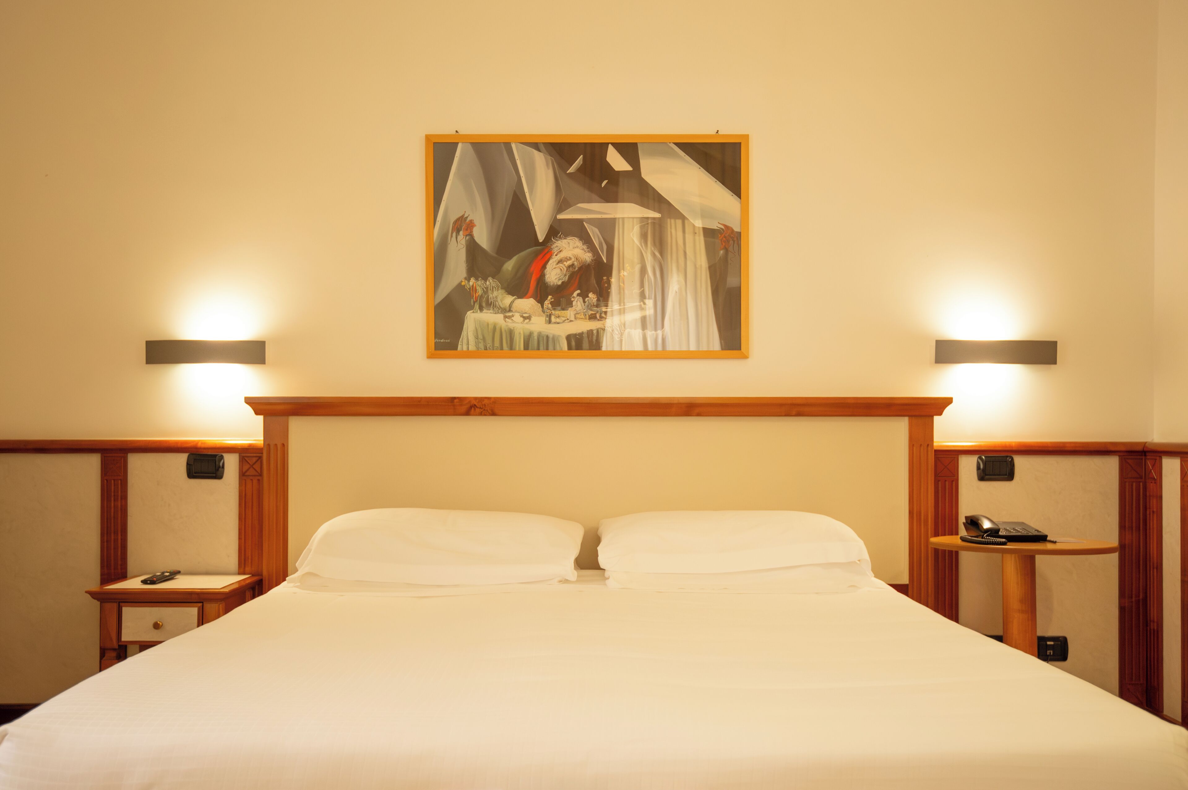 A hotel room with a large bed, two bedside tables, a painting on the wall, and wall-mounted lamps.