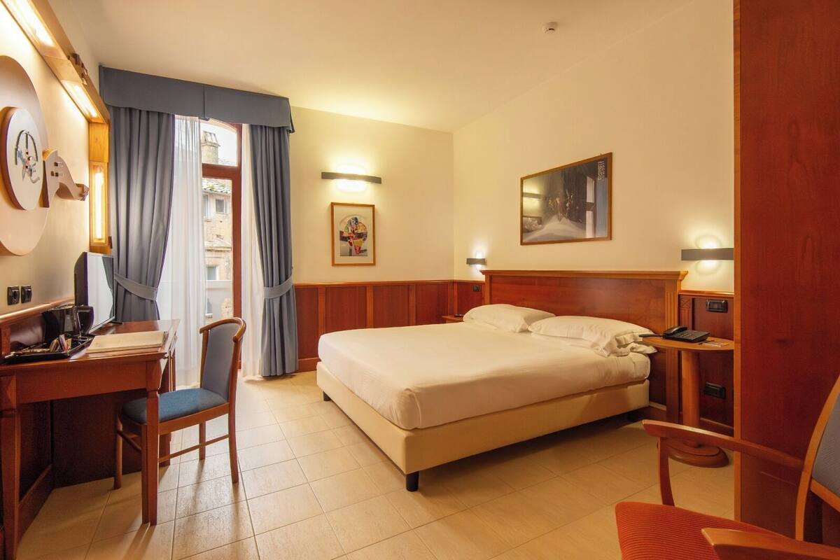 Une chambre d’hôtel avec un lit, un bureau, une chaise et un tableau au mur.