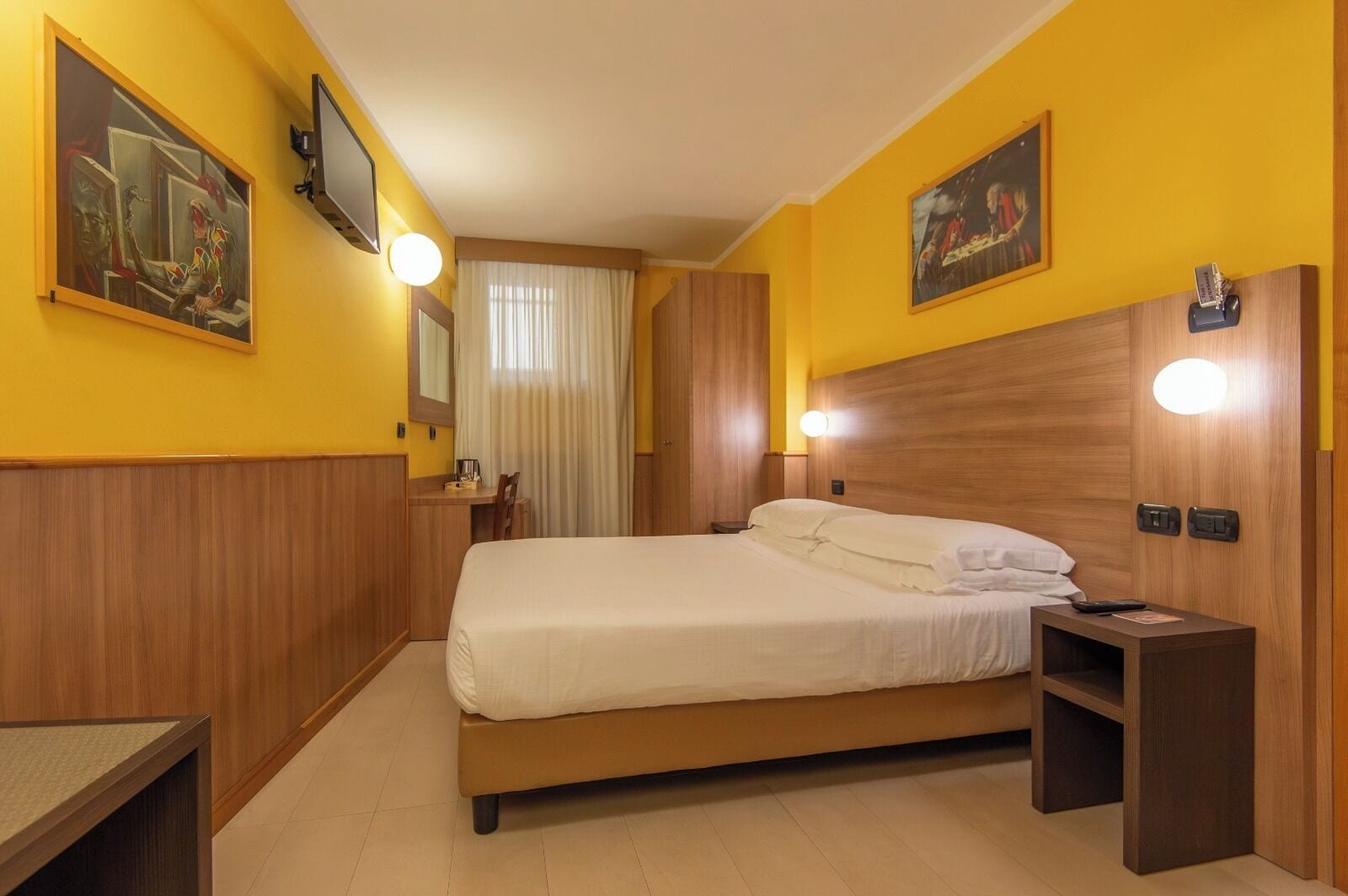 A hotel room with a bed, bedside tables, a desk, and a chair.