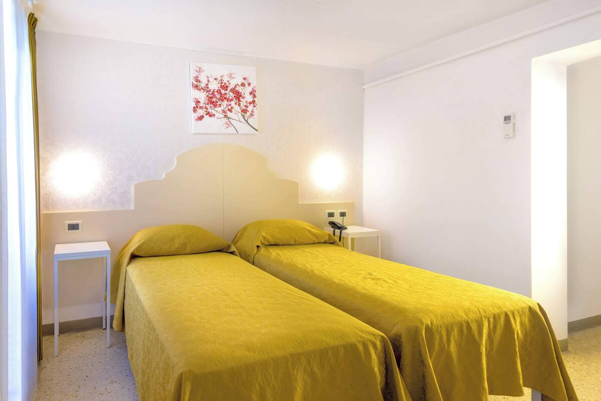 A room with two single beds, a white wall, a small table, a nightstand, and a wall-mounted phone.