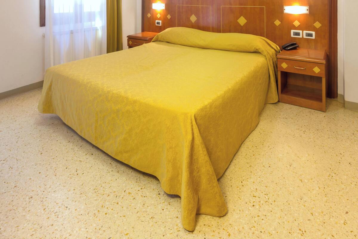 A hotel room with a large bed, wooden headboard, bedside tables, and a telephone.