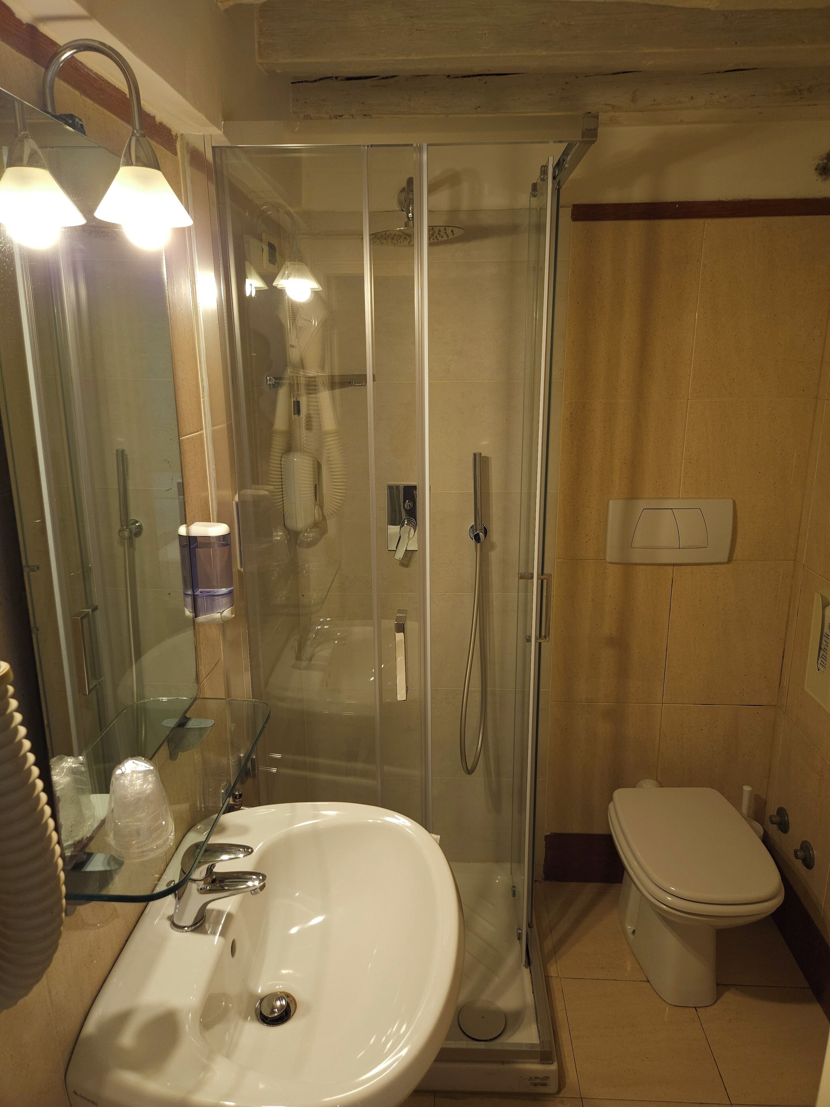 A bathroom with a glass-enclosed shower, a white sink, a toilet, and a mirror with lights.