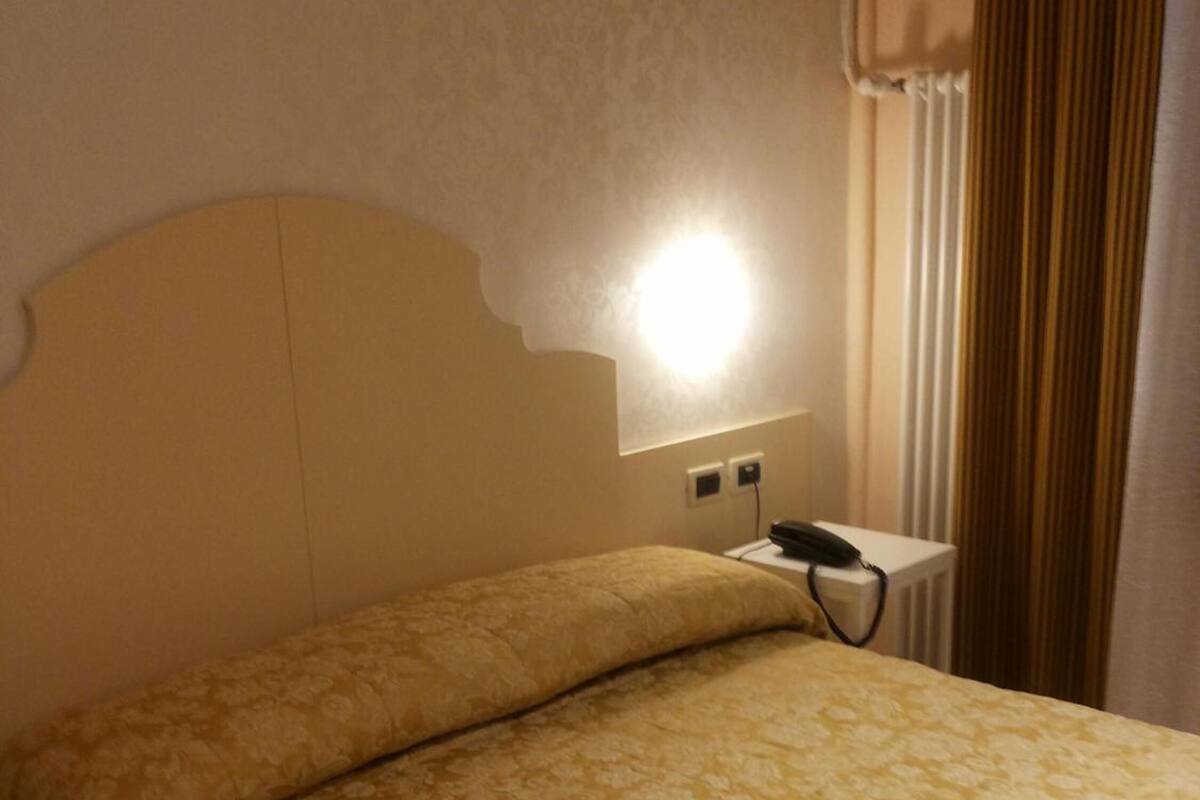 A hotel room with a bed, a bedside table, a lamp, and a window with curtains.